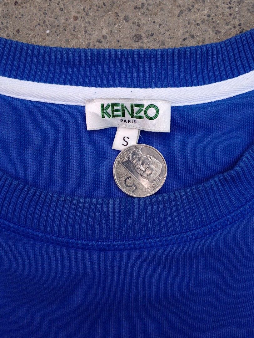Kenzo Paris Blue Sweatshirt Size S (Category: Coats, Jackets and Outerwear) located in Pandi. Submitted by rozz_finds (Listing ID 1470695958, Image 3). Description: - Brand: Kenzo Paris - Style: Blue long sleeve sweatshirt with bold white and black graphic prints on front and back - Size: LENGTH:26 / WIDTH:19 / SLEEVES:26 - Material: 100% cotton, made in Portugal - Condition: Brand new with tags - Care: Machine washable (turn inside out for best 