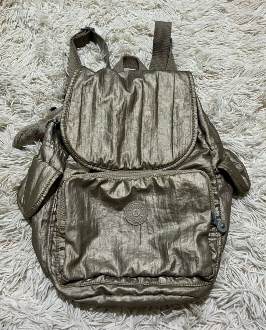 Kipling Metallic Gold Backpack Style K12147-W39 (Category: Backpacks) located in Villasis. Submitted by jinkyreyann (Listing ID 1470617475, Image 1). Description: - Brand: Kipling - Style: Metallic Gold Backpack (Style Code: K12147-W39) - Closure: Flap top with secure drawstring - Pockets: Front zipped pocket and convenient side pockets - Interior: Trendy white and grey checkerboard pattern lining - Extras: Signature Kipling furry monkey keychain