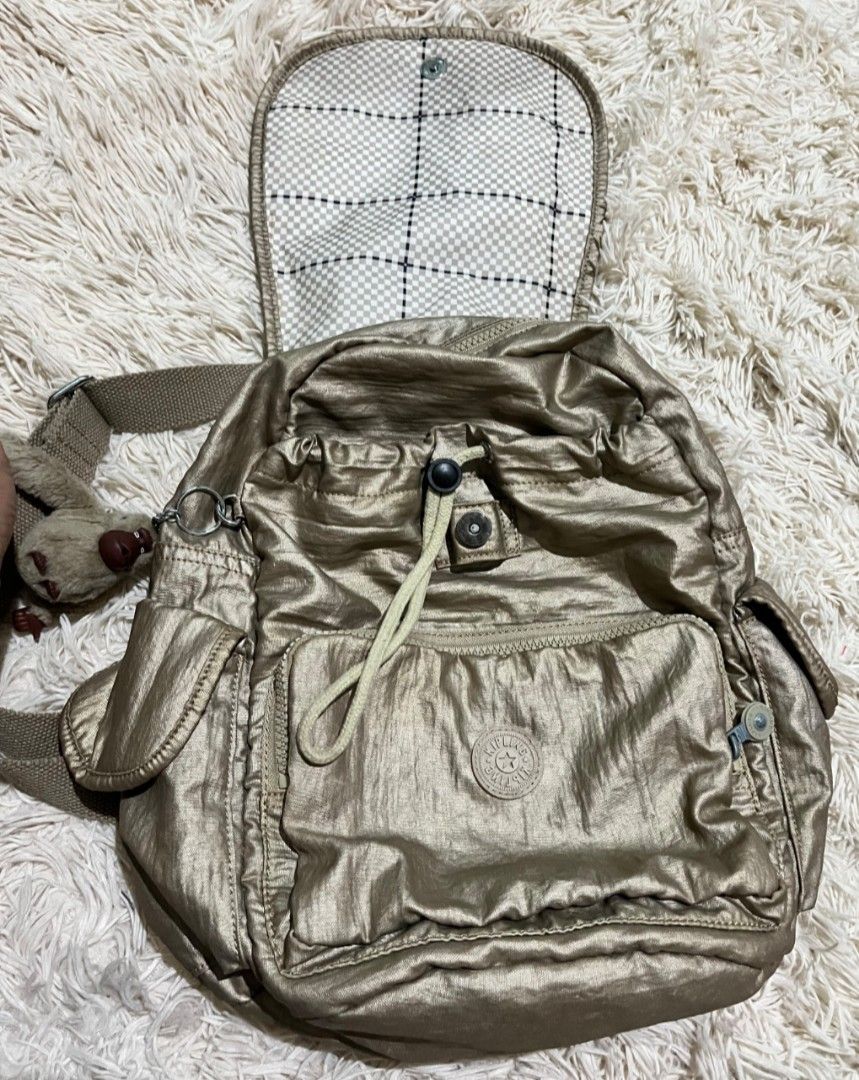 Kipling Metallic Gold Backpack Style K12147-W39 (Category: Backpacks) located in Villasis. Submitted by jinkyreyann (Listing ID 1470617475, Image 2). Description: - Brand: Kipling - Style: Metallic Gold Backpack (Style Code: K12147-W39) - Closure: Flap top with secure drawstring - Pockets: Front zipped pocket and convenient side pockets - Interior: Trendy white and grey checkerboard pattern lining - Extras: Signature Kipling furry monkey keychain