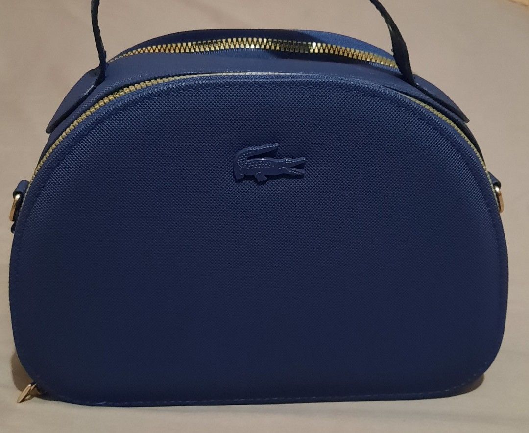 Lacoste Blue Dome Crossbody Bag with Branded Strap (Category: Cross-body Bags) located in Manila. Submitted by gracjam_27 (Listing ID 1470695079, Image 1). Description: - blue Lacoste dome-shaped handbag - Stylish textured finish with elegant gold hardware - Secure double top-zipper closure - Clean dark blue interior lining - Includes a matching adjustable blue strap with bold white Lacoste branding - Versatile design: wear by the top handle or a