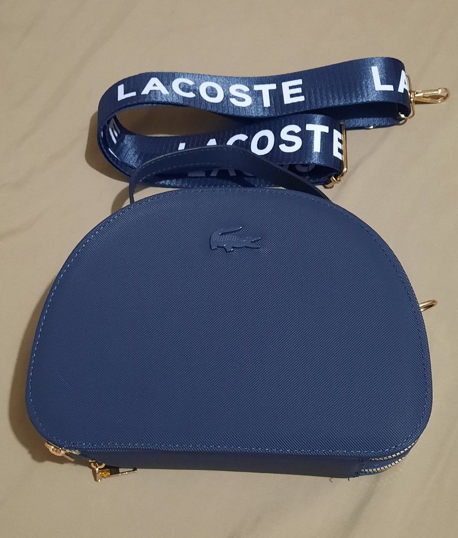 Lacoste Blue Dome Crossbody Bag with Branded Strap (Category: Cross-body Bags) located in Manila. Submitted by gracjam_27 (Listing ID 1470695079, Image 2). Description: - blue Lacoste dome-shaped handbag - Stylish textured finish with elegant gold hardware - Secure double top-zipper closure - Clean dark blue interior lining - Includes a matching adjustable blue strap with bold white Lacoste branding - Versatile design: wear by the top handle or a