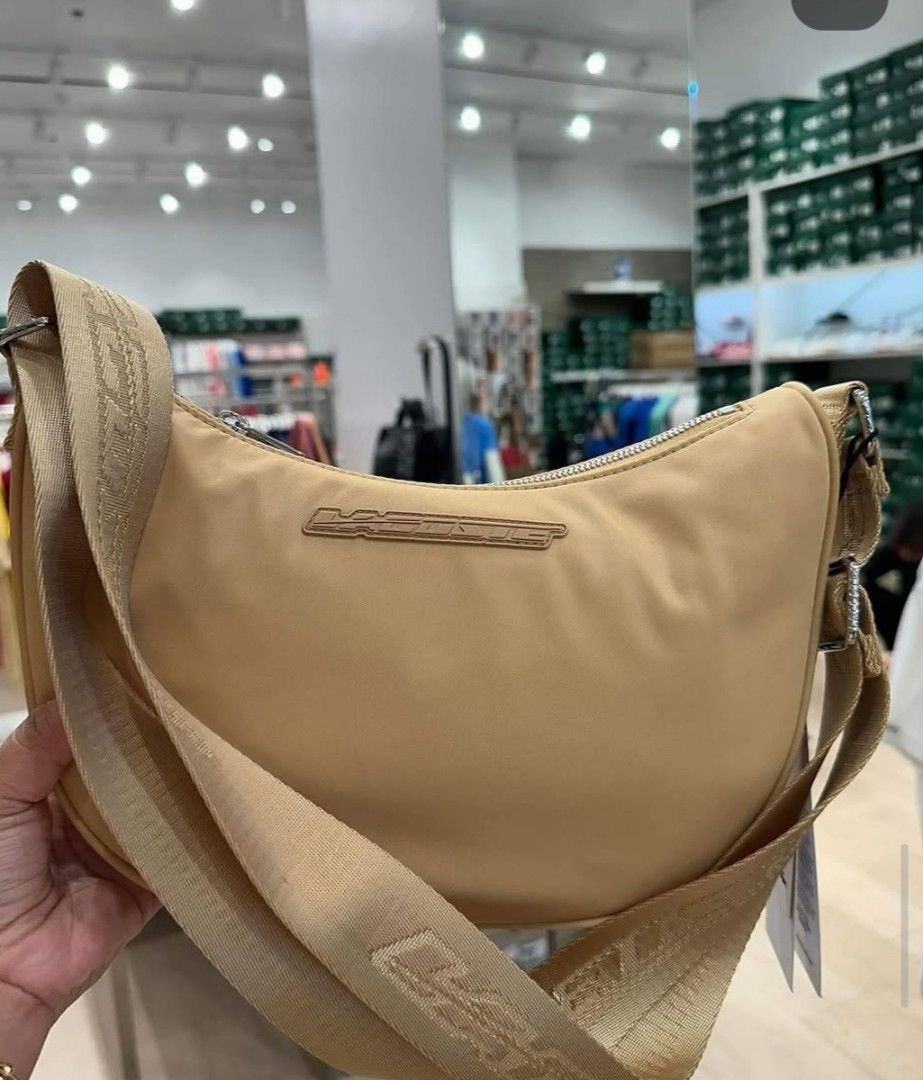Lacoste Moon Bag Beige Crossbody (Category: Cross-body Bags) located in Polomolok. Submitted by legadad94559 (Listing ID 1470701760, Image 3). Description: - Authentic Lacoste moon bag in a versatile neutral beige shade - Durable nylon material with a chic, structured curved shape - Thick adjustable strap with stylish printed Lacoste lettering - Secure zip top closure to keep your essentials safe - Iconic metal logo plaque centered on the front -