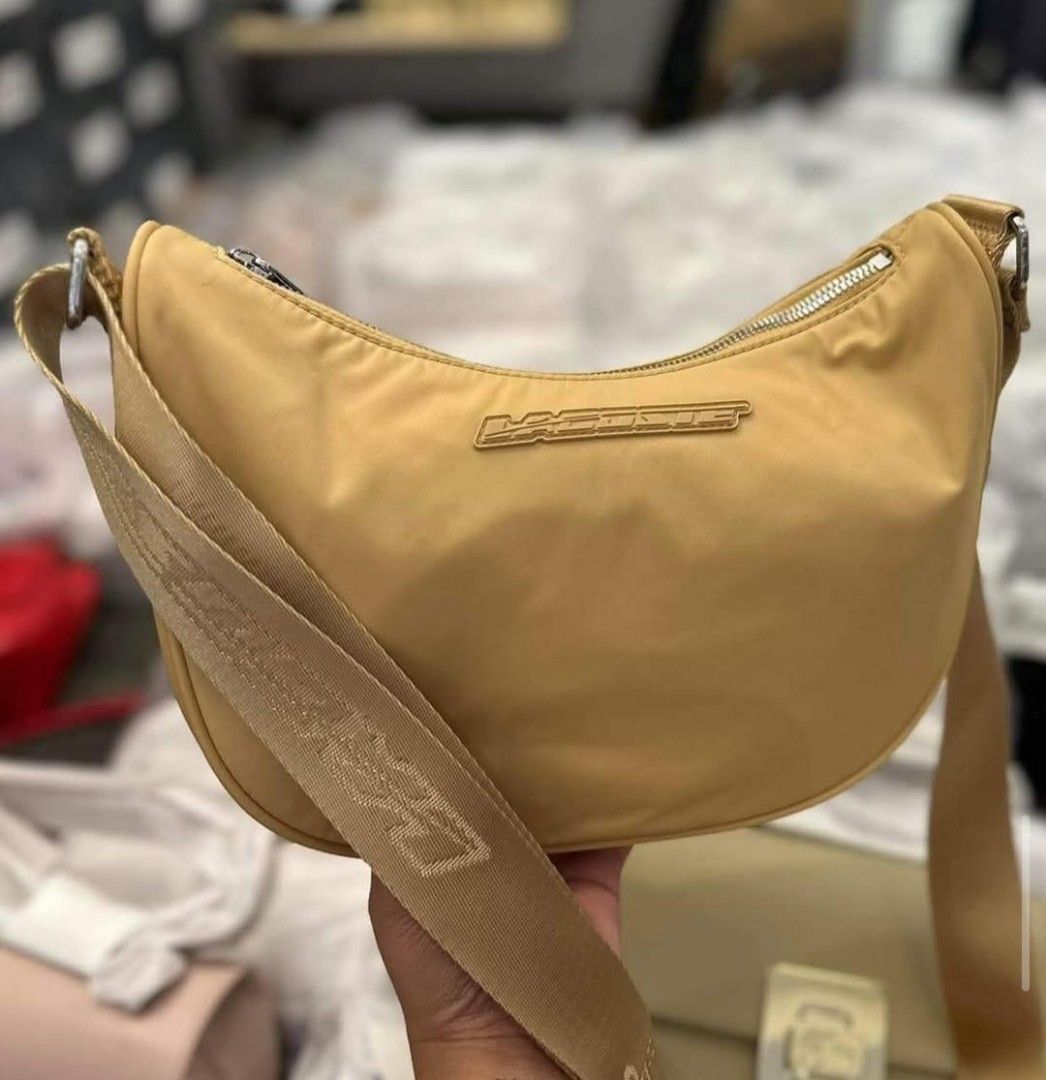 Lacoste Moon Bag Beige Crossbody (Category: Cross-body Bags) located in Polomolok. Submitted by legadad94559 (Listing ID 1470701760, Image 2). Description: - Authentic Lacoste moon bag in a versatile neutral beige shade - Durable nylon material with a chic, structured curved shape - Thick adjustable strap with stylish printed Lacoste lettering - Secure zip top closure to keep your essentials safe - Iconic metal logo plaque centered on the front -