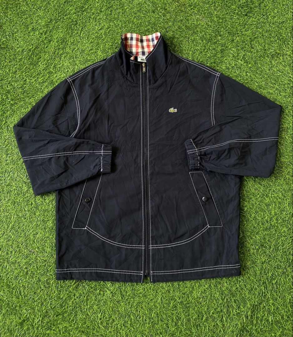 Lacoste Navy Blue Windbreaker Jacket Size 95 (Category: Coats, Jackets and Outerwear) located in Manila. Submitted by clevermountain_9c1516 (Listing ID 1470661586, Image 1). Description: - Brand: Lacoste - Color: Dark navy blue with white contrast stitching - Design details: Red, white, and navy checkered inner collar, striking white text and logo graphic on the back - Pockets: Two front pockets with secure button flaps - Fit & Comfort: Elastic c