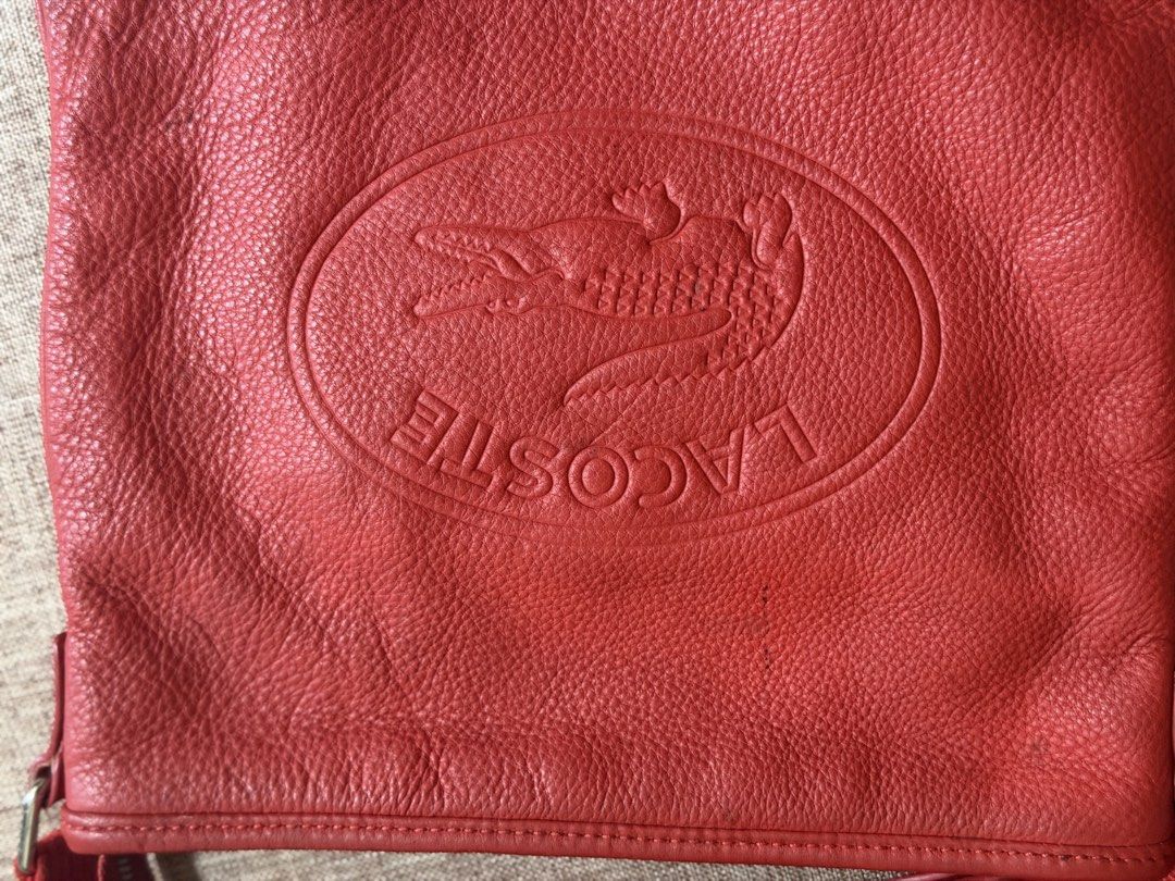 Lacoste Red Leather Crossbody Bag (Category: Cross-body Bags) located in Taguig. Submitted by markitopinas (Listing ID 1470618792, Image 2). Description: - Brand: Lacoste - Style: Red leather crossbody bag with debossed crocodile logo - Size: Medium (fits daily essentials) - Strap: Adjustable red canvas strap - Closure & Interior: Zip top closure, dark fabric lining, interior zippered pocket, and leather brand tag - Condition: Minor creasing on t