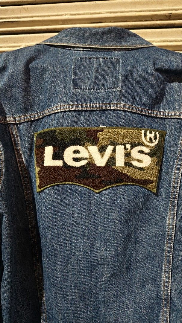 Levi's Denim Trucker Jacket Size M (Category: Coats, Jackets and Outerwear) located in Quezon City. Submitted by truedeer_cda94c (Listing ID 1470606011, Image 3). Description: - Brand: Levi's - Style: Denim jacket with classic button-up front, chest pockets, and side pockets - Color/Wash: Medium blue wash - Size: Medium (M) - Special Feature: Textured camouflage Levi's logo patch stitched across the back - Details: Includes interior wash tags and