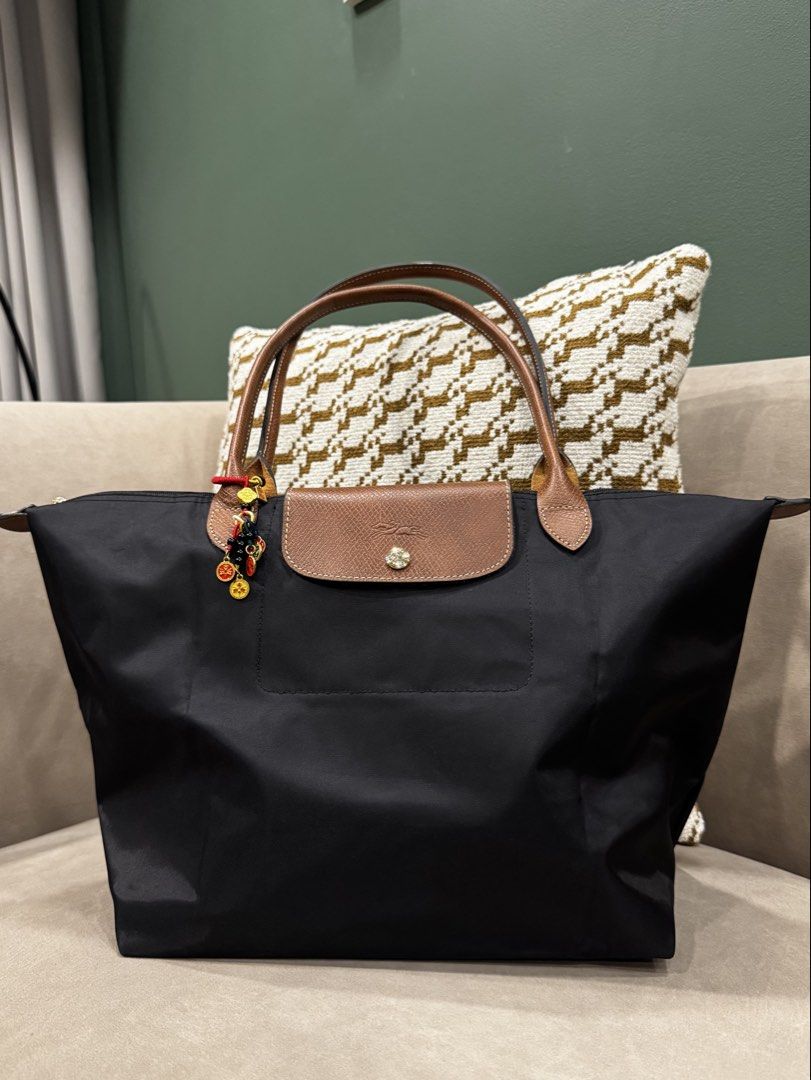 Longchamp Le Pliage Nylon Tote Bag Black (Category: Luxury Bags & Wallets) located in Manila. Submitted by love_preloveddd (Listing ID 1470657092, Image 1). Description: - Longchamp tote bag in classic black - Medium size with brown leather handles and top flap - Secure snap closure with gold-tone hardware - Includes a decorative charm with colorful beads and gold coins - Lightweight, durable nylon body that folds flat easily - Clean interior lin