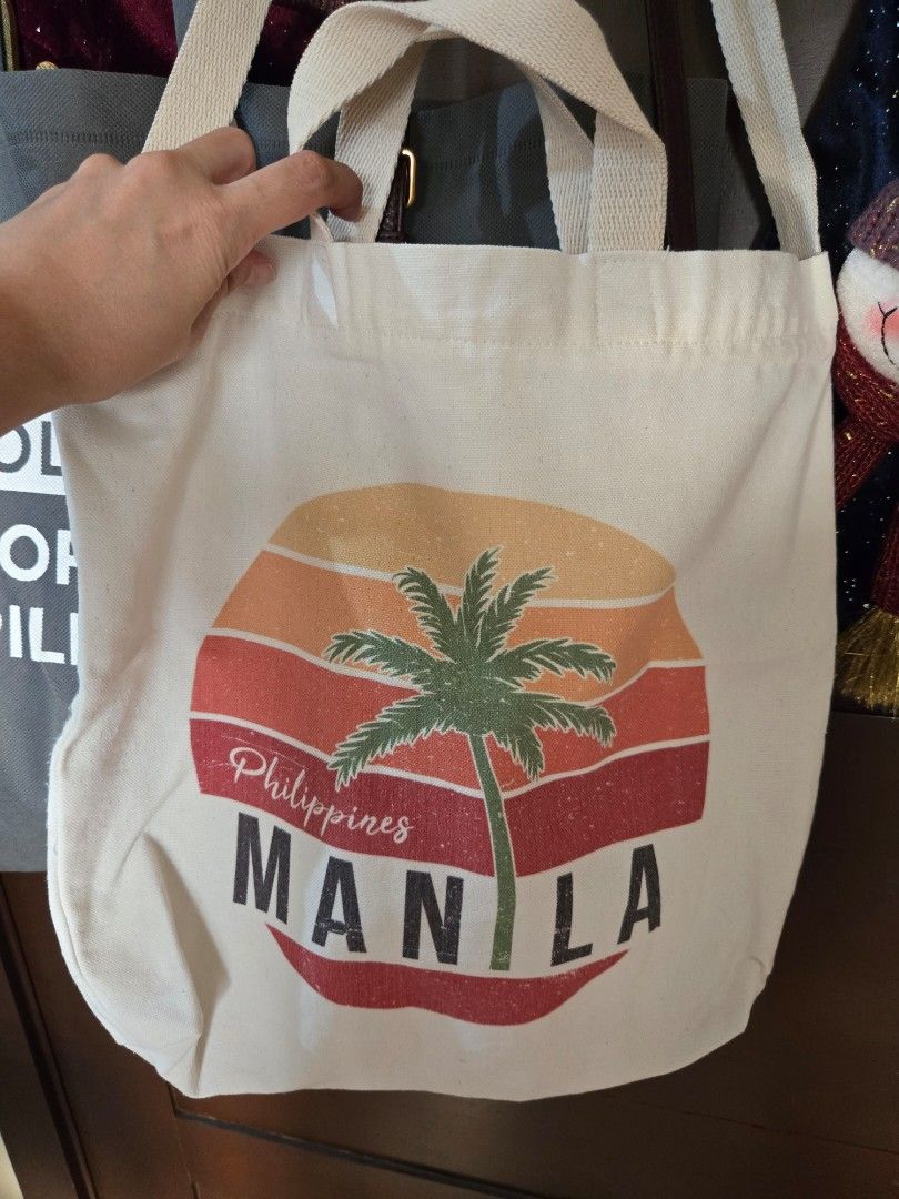 Manila Philippines Palm Tree Canvas Tote Bag (Category: Tote Bags) located in Quezon City. Submitted by mgdeclutters (Listing ID 1470576726, Image 2). Description: - Material: Durable neutral cream canvas fabric - Design: Stylish Manila, Philippines graphic with sunset stripes and palm tree artwork - Straps: Comfortable double fabric handles for easy carrying - Versatility: Ideal casual everyday bag for groceries, books, or beach days - Condition