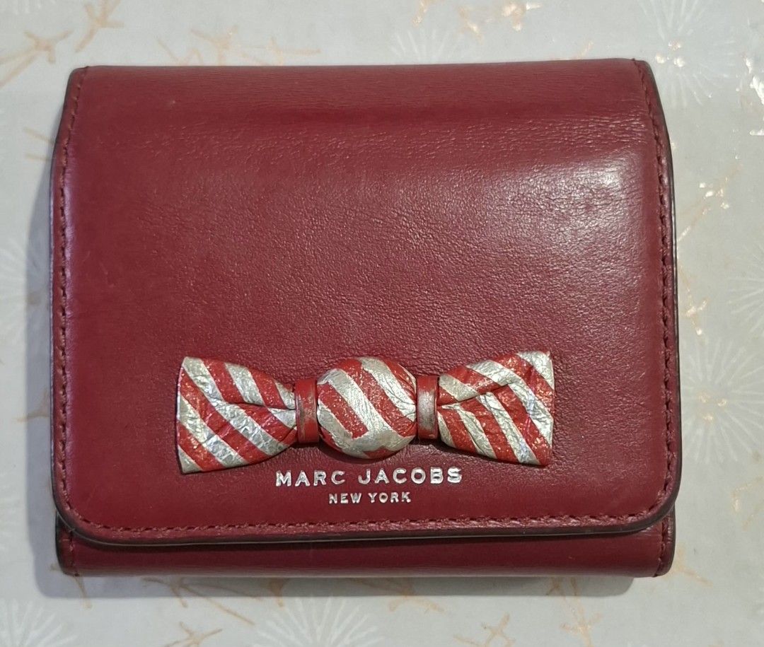 Marc Jacobs Red Leather Bow Wallet (Category: Luxury Bags & Wallets) located in Don Carlos. Submitted by PphiXi_Finds (Listing ID 1470726745, Image 1). Description: - Brand: Marc Jacobs New York - Material: Genuine red leather - Design: Compact trifold with snap closure - Features: Card slots, cash compartment, and zipped coin pocket - Accents: Unique striped silver and red bow hardware on the front flap - Condition: Minor wear along the edges an