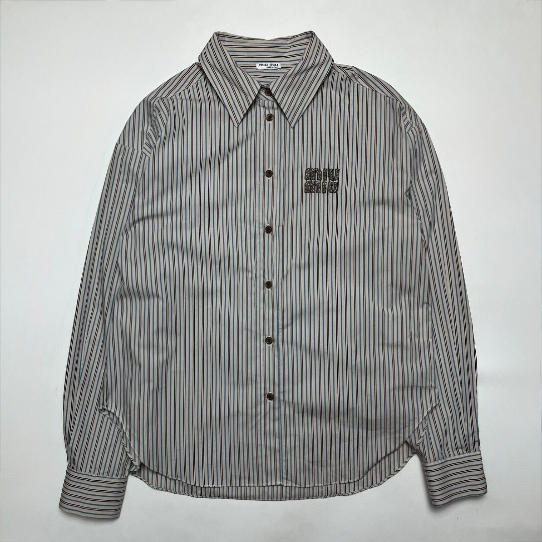 Miu Miu Striped Button-Down Shirt (Category: Shirts) located in Caloocan City. Submitted by achilles_grails (Listing ID 1470727452, Image 1). Description: - Brand: Miu Miu - Style: Long-sleeve button-down shirt - Pattern: Beige, blue, and black stripes - Size: S (Made in Italy) - Material: 100% Cotton - Details: Classic pointed collar, front button closure, brown embroidered logo patch on chest, buttoned cuffs - Condition: Clean, excellent overal