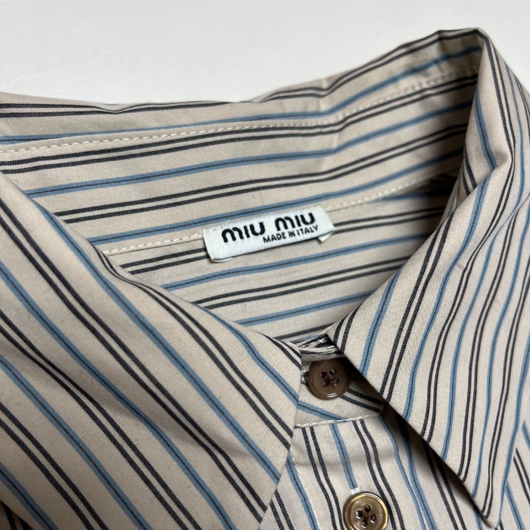 Miu Miu Striped Button-Down Shirt (Category: Shirts) located in Caloocan City. Submitted by achilles_grails (Listing ID 1470727452, Image 3). Description: - Brand: Miu Miu - Style: Long-sleeve button-down shirt - Pattern: Beige, blue, and black stripes - Size: S (Made in Italy) - Material: 100% Cotton - Details: Classic pointed collar, front button closure, brown embroidered logo patch on chest, buttoned cuffs - Condition: Clean, excellent overal
