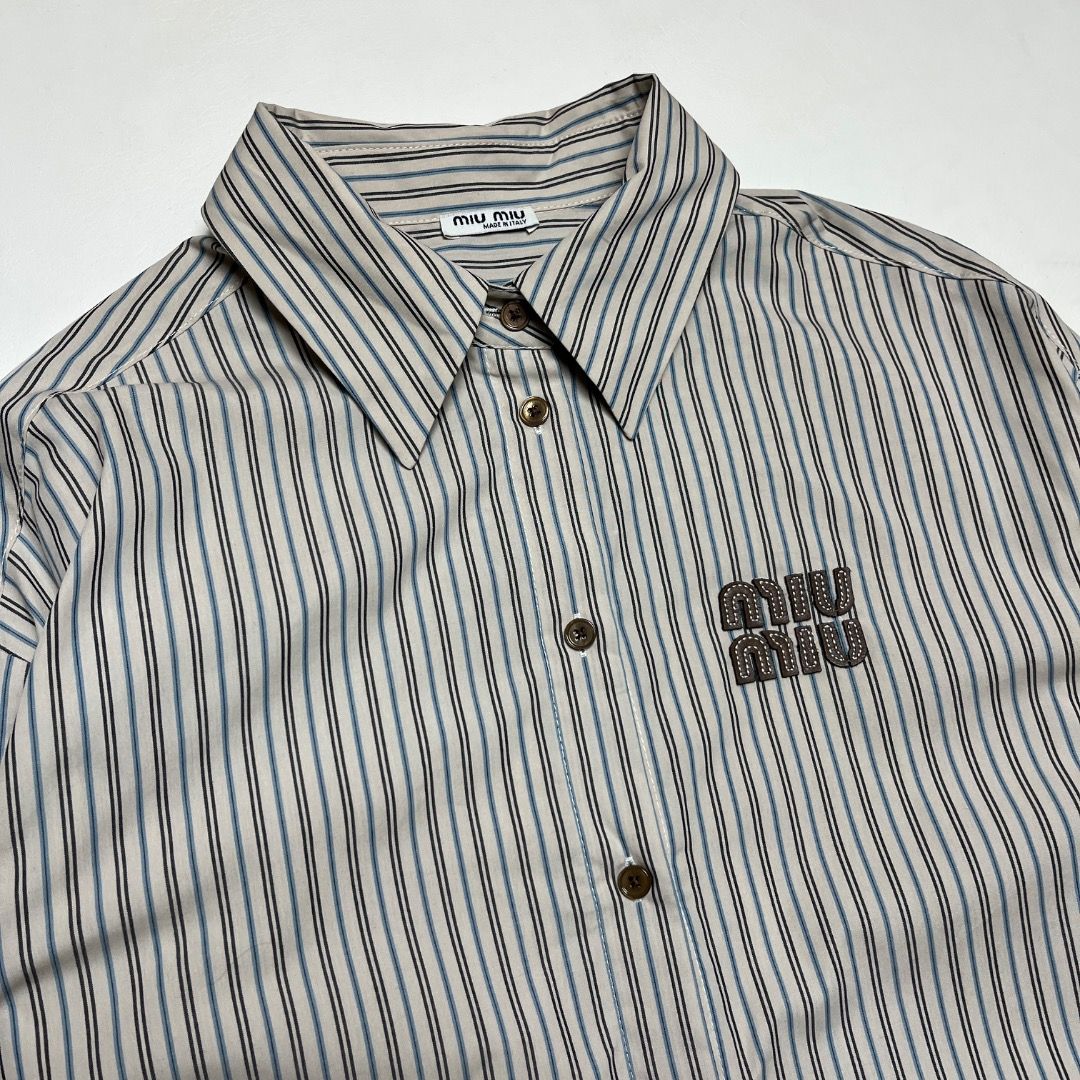 Miu Miu Striped Button-Down Shirt (Category: Shirts) located in Caloocan City. Submitted by achilles_grails (Listing ID 1470727452, Image 2). Description: - Brand: Miu Miu - Style: Long-sleeve button-down shirt - Pattern: Beige, blue, and black stripes - Size: S (Made in Italy) - Material: 100% Cotton - Details: Classic pointed collar, front button closure, brown embroidered logo patch on chest, buttoned cuffs - Condition: Clean, excellent overal