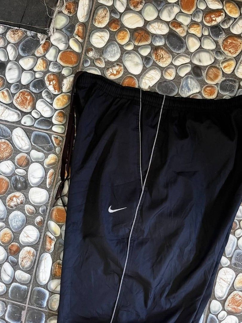 Nike Black Track Pants (Category: Joggers) located in Baler. Submitted by vansonearth (Listing ID 1470700939, Image 3). Description: - Color: Classic black with white side piping - Fit: Straight leg with a relaxed, loose styling - Material: Lightweight nylon for ultimate comfort - Waistband: Elastic with an adjustable drawstring - Branding: Embroidered white Nike Swoosh logo on the front left hip - Storage: Convenient single rear pocket on the ba