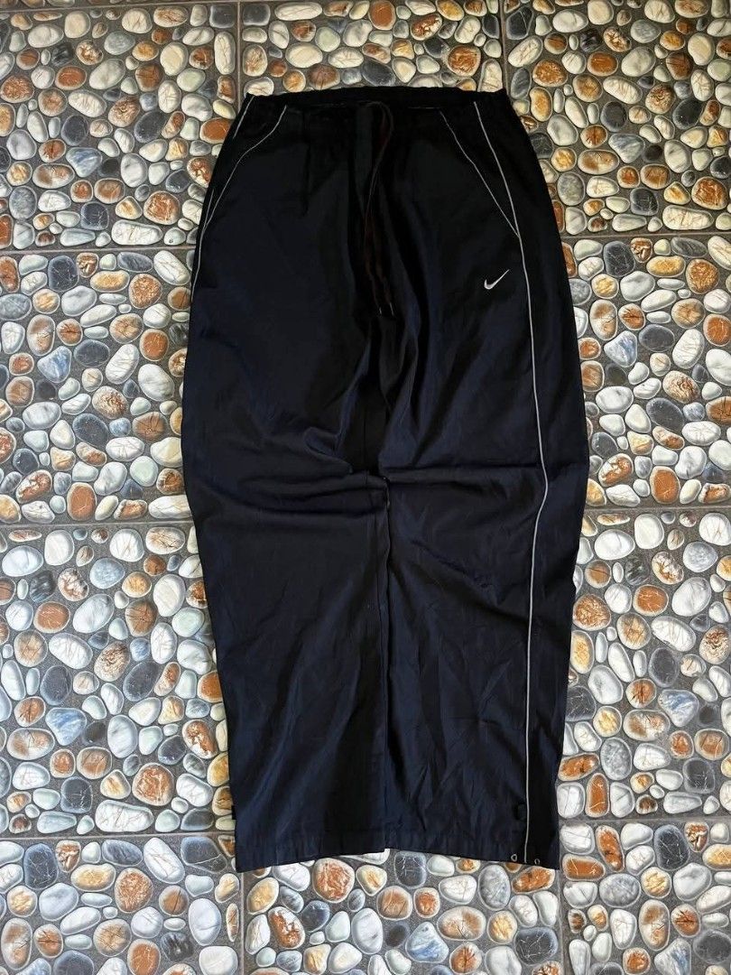 Nike Black Track Pants (Category: Joggers) located in Baler. Submitted by vansonearth (Listing ID 1470700939, Image 1). Description: - Color: Classic black with white side piping - Fit: Straight leg with a relaxed, loose styling - Material: Lightweight nylon for ultimate comfort - Waistband: Elastic with an adjustable drawstring - Branding: Embroidered white Nike Swoosh logo on the front left hip - Storage: Convenient single rear pocket on the ba