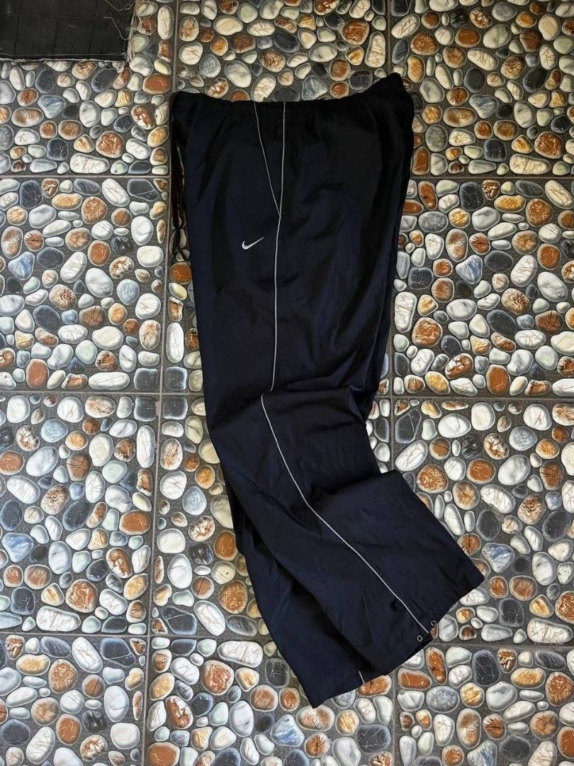 Nike Black Track Pants (Category: Joggers) located in Baler. Submitted by vansonearth (Listing ID 1470700939, Image 2). Description: - Color: Classic black with white side piping - Fit: Straight leg with a relaxed, loose styling - Material: Lightweight nylon for ultimate comfort - Waistband: Elastic with an adjustable drawstring - Branding: Embroidered white Nike Swoosh logo on the front left hip - Storage: Convenient single rear pocket on the ba