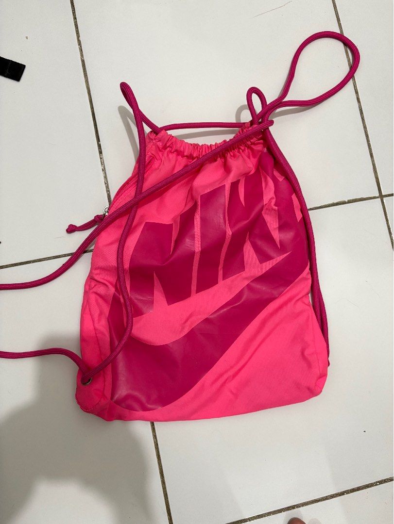 Nike Pink Drawstring Gym Bag (Category: Backpacks) located in Taguig. Submitted by cftbncs (Listing ID 1470560823, Image 1). Description: - Authentic bright pink Nike drawstring bag - Large stacked logo graphic on the front - Side zipper pocket for secure storage of small essentials - Thick, durable drawstring cords for easy closure - Clean interior lining with fabric tag - Lightweight and versatile for workouts or daily use.