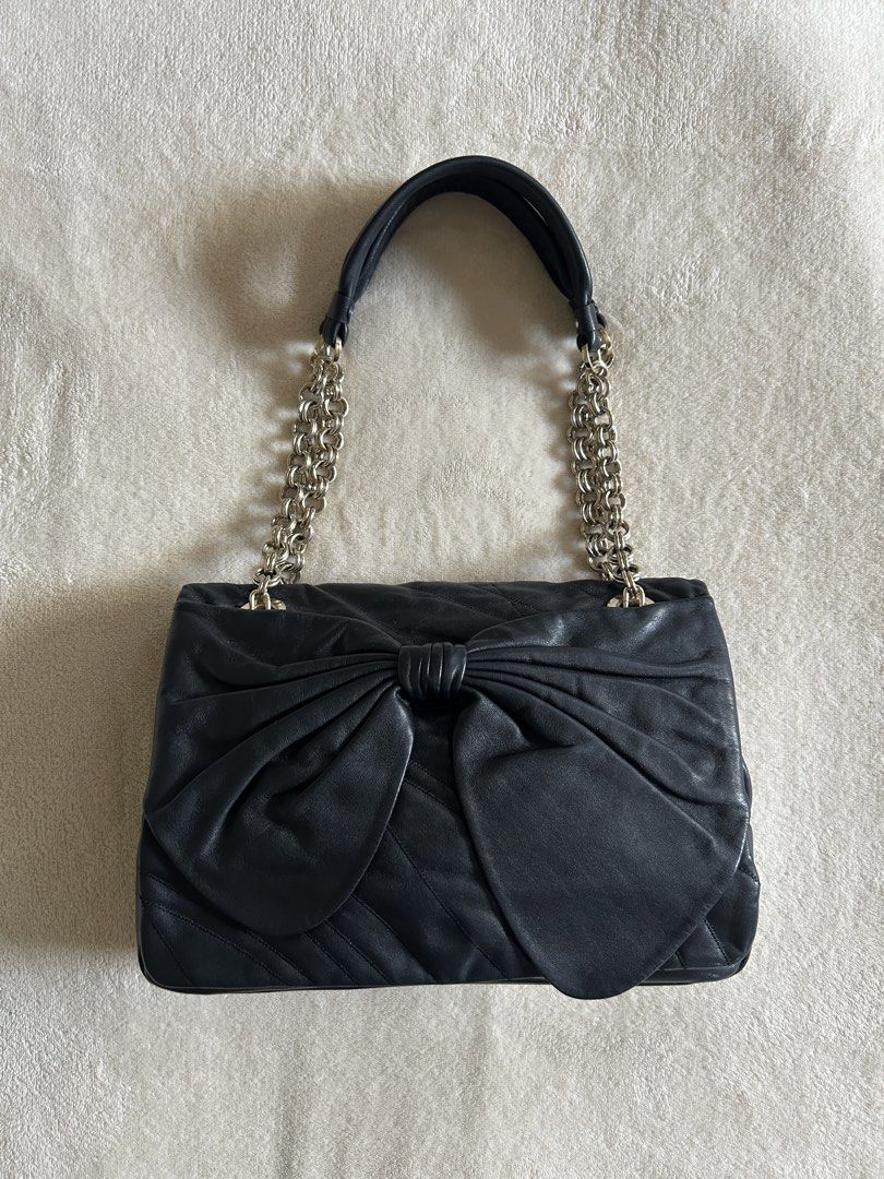 Nina Ricci Leather Bow Flap Bag (Category: Shoulder Bags) located in Carigara. Submitted by abiesclutter (Listing ID 1470627426, Image 1). Description: Brand: Nina Ricci Design: A black leather shoulder bag featuring a pleated bow detail on the full front flap, very practical back pocket and twin shoulder straps. Spacious internal and a zipper compartment. Hardware: Silver Dimension: - Length: 26 cm - Width: 8 cm - Height: 18 cm - Handle Drop: 21