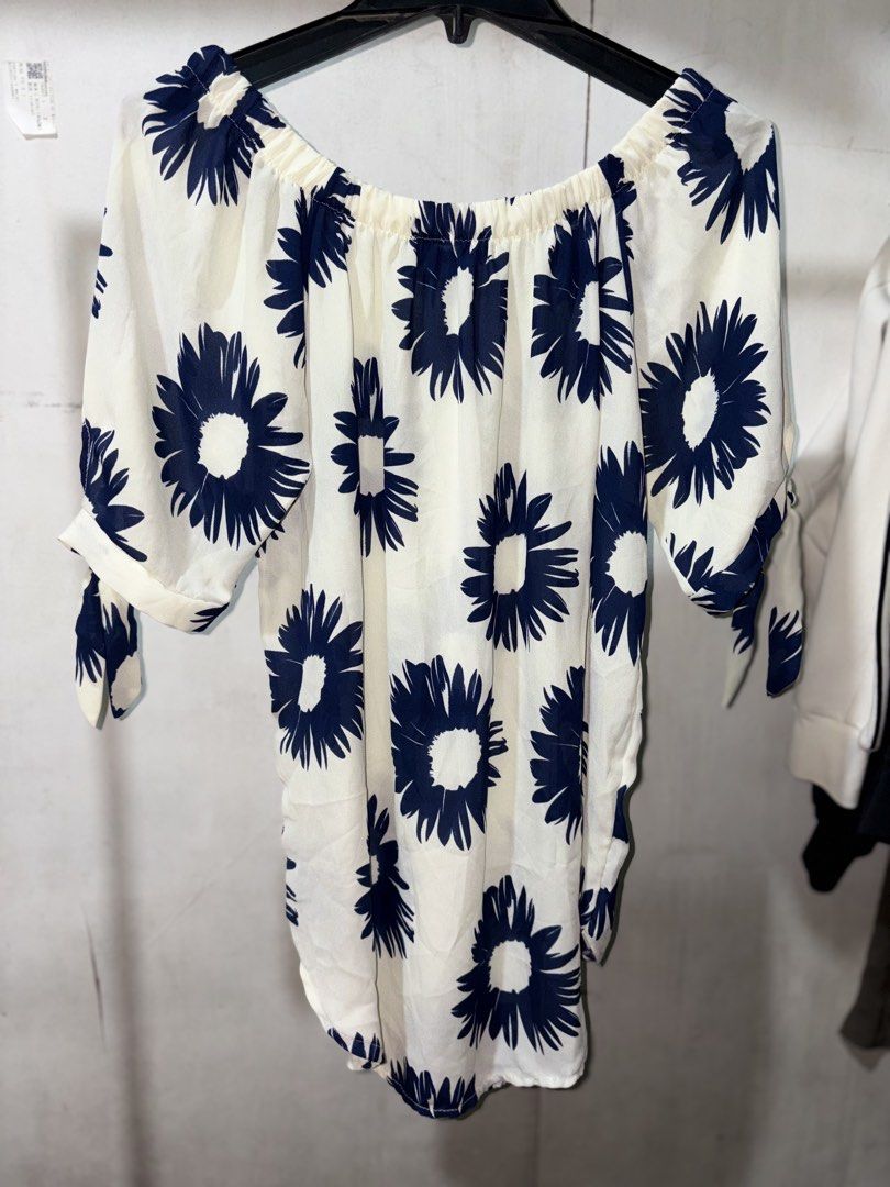 Off-shoulder white blouse with blue floral print (Category: Blouses) located in Cavite. Submitted by earthread (Listing ID 1470660539, Image 1). Description: - Style: Off-shoulder top with half sleeves - Design: All-over navy blue sunflower pattern and cute tie-knot cuffs - Comfort: Elastic neckline for a secure, comfortable fit - Fabric: Lightweight and breathable, ideal for warm weather - Versatility: Easy to pair with your favorite denim short