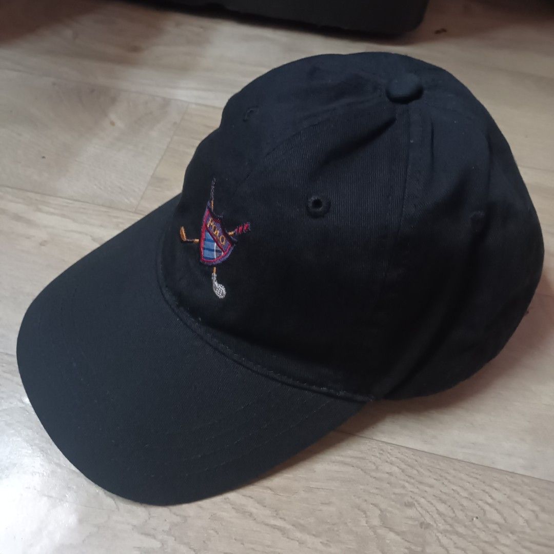 Polo Golf Ralph Lauren Cap (Category: Caps & Hats) located in Manila. Submitted by itsnik444 (Listing ID 1470641200, Image 2). Description: - Brand: Polo Golf Ralph Lauren - Color: Black - Design: Embroidered shield logo with golf clubs and plaid pattern on front - Closure: Adjustable strap back with engraved metal buckle - Details: Interior brand label and care tag intact, standard curved brim - Condition: Clean fabric, great for the course or d