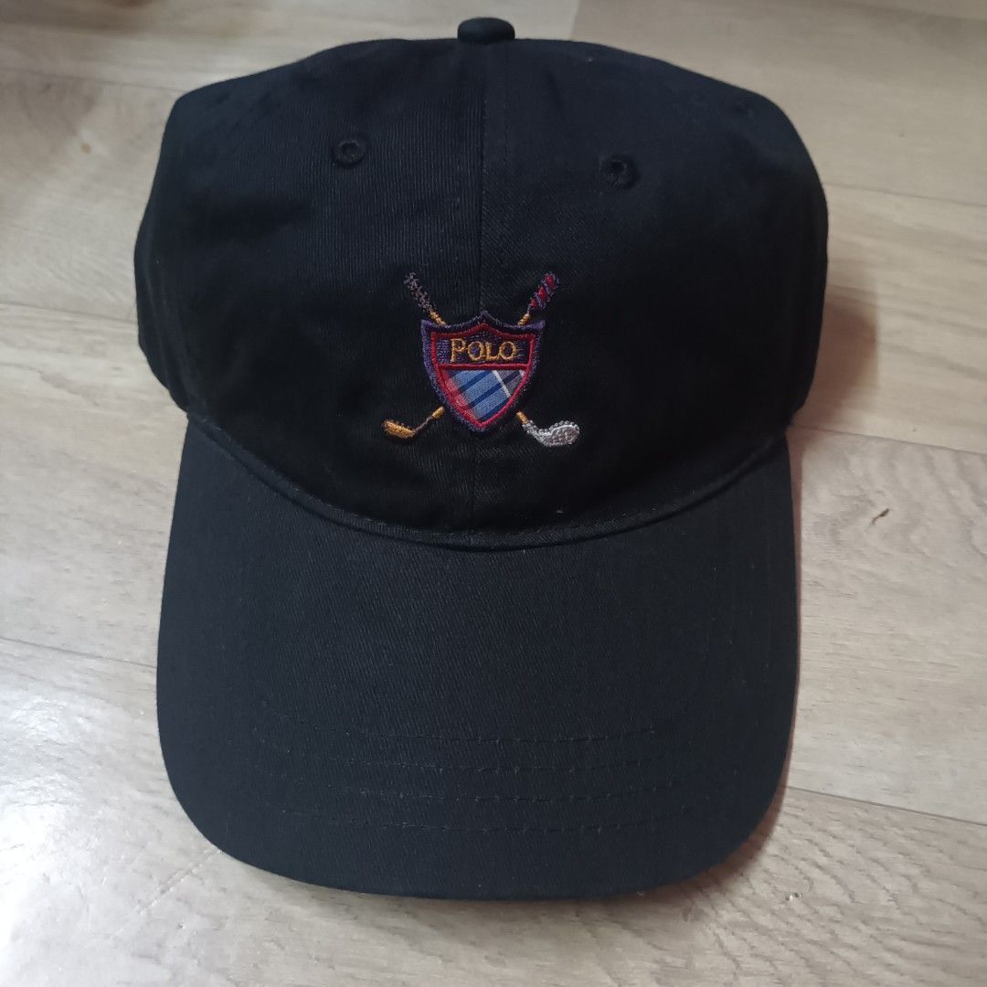 Polo Golf Ralph Lauren Cap (Category: Caps & Hats) located in Manila. Submitted by itsnik444 (Listing ID 1470641200, Image 1). Description: - Brand: Polo Golf Ralph Lauren - Color: Black - Design: Embroidered shield logo with golf clubs and plaid pattern on front - Closure: Adjustable strap back with engraved metal buckle - Details: Interior brand label and care tag intact, standard curved brim - Condition: Clean fabric, great for the course or d