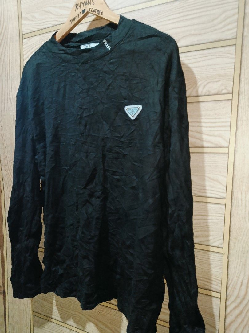 Prada Black Long Sleeve Sweater with Logo Patch (Category: Coats, Jackets and Outerwear) located in Narra. Submitted by rhyanguan63087 (Listing ID 1470628655, Image 2). Description: - Brand: Prada - Color: Black - Material: Soft, comfortable cotton - Design: Crew neckline with subtle collar embroidery - Logo: Signature light blue triangle metal logo patch on the left chest - Details: Prada Milano inner tag and care label - Condition: Clean and re