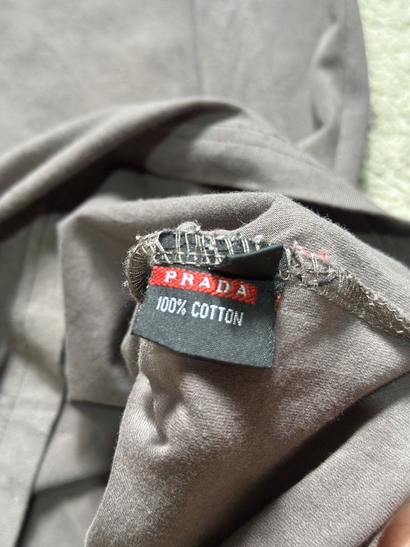 Prada Grey Long Sleeve T-Shirt (Category: Longsleeves) located in Daet. Submitted by thrifthings2018 (Listing ID 1470618422, Image 3). Description: - Brand: Prada - Item: Long sleeve tee - Color: Dark grey - Material: 100% cotton - Design: Bold distressed Prada logo across the chest with signature red Prada tag on hem and inner collar - Measurements: Width 20 inches, Length 27 inches - Care: Machine wash warm - Condition: Excellent / Well-maintai
