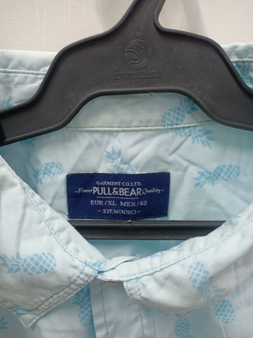 Pull&Bear Light Blue Pineapple Print Short Sleeve Shirt XL (Category: Tshirts & Polo Shirts ) located in Bayombong. Submitted by rheaaa00530 (Listing ID 1470672712, Image 2). Description: - Brand: Pull&Bear - Style: Short-sleeve button-up shirt with classic collar and left chest pocket - Color/Design: Light blue with all-over pineapple print - Size: EUR/XL / MEX/42 - Fit: Regular fit - Condition: Great casual piece for warm weather.