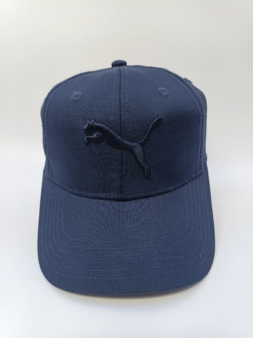 Puma Navy Blue Embroidered Logo Baseball Cap OSFA (Category: Caps & Hats) located in Imus. Submitted by grindhouse.thriftshop (Listing ID 1470606889, Image 1). Description: - Brand: Puma - Color: Navy blue - Design: Embroidered leaping cat logo on the front - Fit: One size fits all with an adjustable back strap - Material: 100% polyester body, 100% cotton sunshade back - Details: Branded interior taping along the seams - Condition: Clean inside a