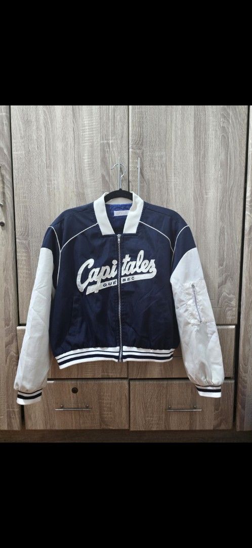 Quebec Capitales Varsity Bomber Jacket Navy White (Category: Coats, Jackets and Outerwear) located in Manila. Submitted by cee_gotaway6991 (Listing ID 1470689569, Image 1). Description: - Color: Navy blue body with contrasting white sleeves - Design: Quebec Capitales embroidered text across the chest - Details: Front zip closure and sleeve utility zip pocket on the left arm - Trim: White striped collar, cuffs, and hem - Fit: Bomber silhouette wit