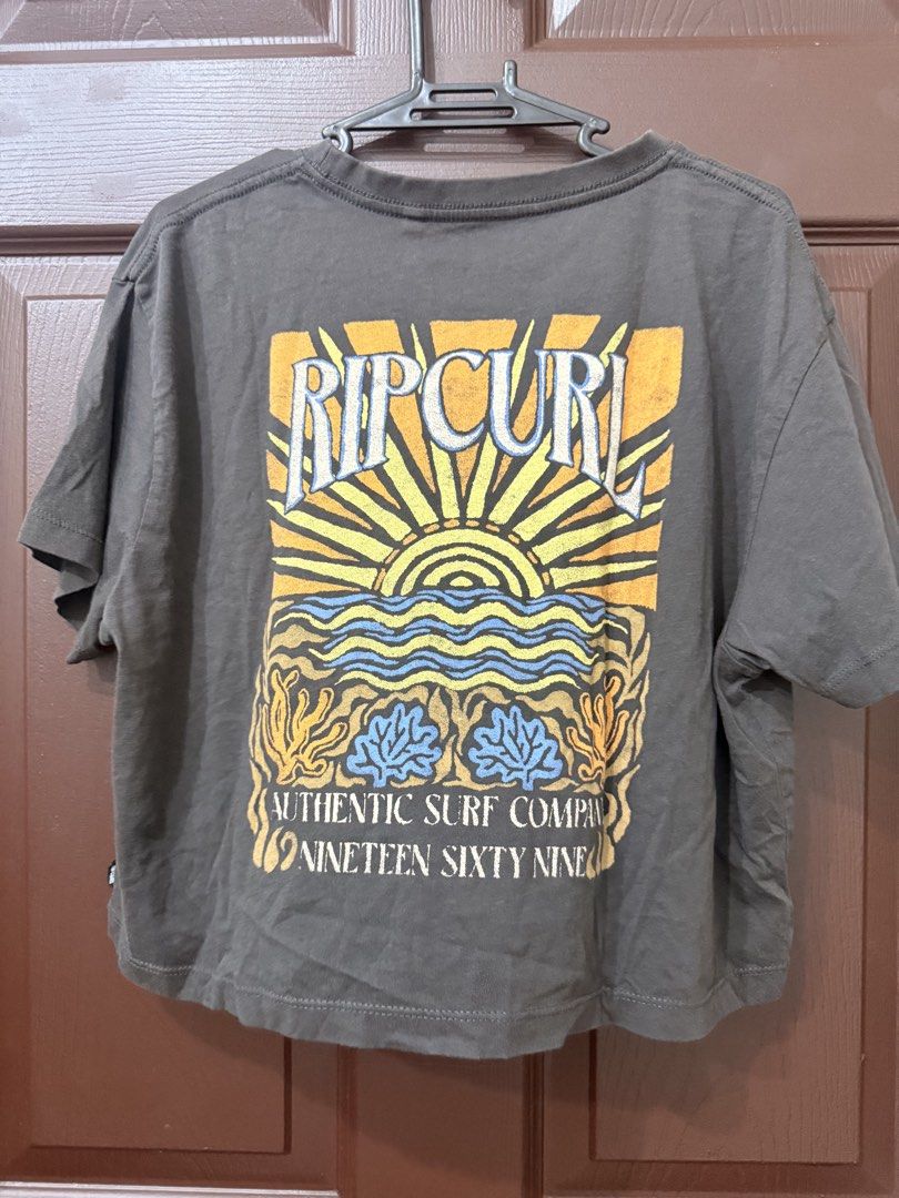 Rip Curl Graphic Surf Tee (Category: Shirts) located in Pasay City. Submitted by annythingz28 (Listing ID 1470666188, Image 2). Description: - Brand: Rip Curl - Color: Dark Grey - Size: Small - Design: Small logo on front left chest; large vintage sun, wave, and floral graphic on the back - Fit: Relaxed crew neck with short sleeves - Style: Casual everyday surf wear, comfortable fit - Condition: Excellent / Pre-loved (ready to wear).