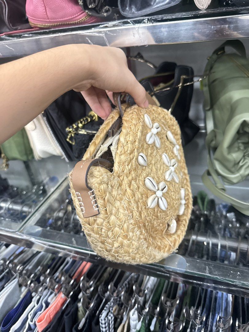 Round Straw Crossbody Bag with Seashells (Category: Cross-body Bags) located in Abucay. Submitted by fastlion.584bdf (Listing ID 1470649053, Image 2). Description: - Style: Round woven straw crossbody bag - Details: White seashell flower motifs on the front - Features: Tan leatherette strap attachments and secure zipper closure - Size: Compact, perfect for summer outfits and beach days - Condition: Clean inside and out, ready to use.