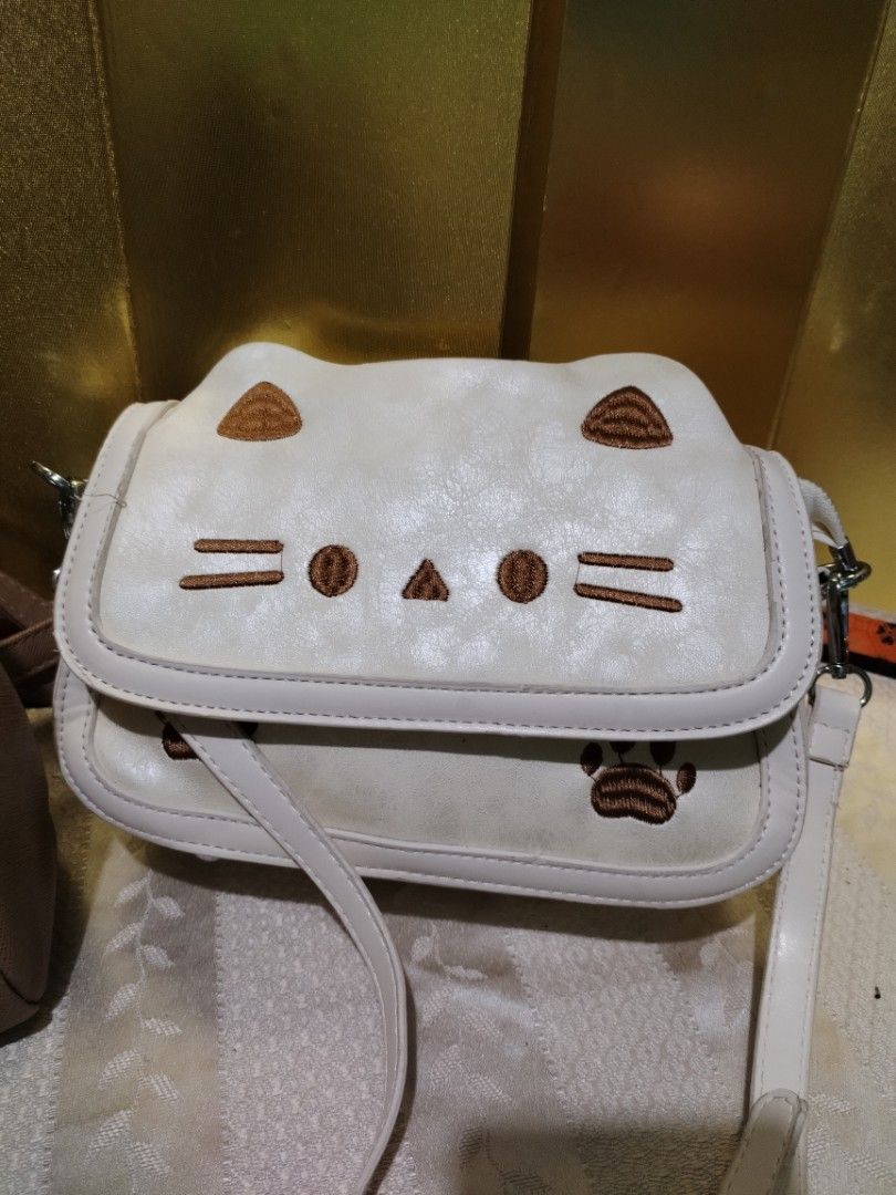 Secosana brown backpack and white cat sling bag (Category: Backpacks) located in La Trinidad. Submitted by malditas (Listing ID 1470705989, Image 2). Description: - 2-in-1 bag bundle in clean, ready-to-use condition - Secosana brown backpack featuring a handy front zipper pocket and metallic logo plate - White sling bag adorned with an adorable embroidered cat face and paw prints on the flap - Sling bag comes with an adjustable strap for comforta