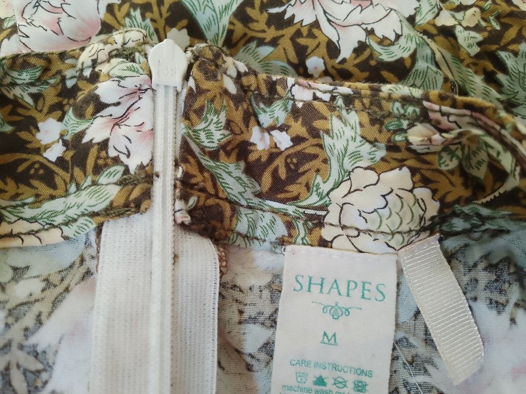 SHAPES Floral Mini Skirt Size M (Category: Skirts) located in Valenzuela. Submitted by kn.sell (Listing ID 1470615773, Image 3). Description: - Brand/Style: Shapes short floral skirt - Size: Medium - Design: Brown background with pink/cream flowers and green leaves - Details: Back zipper closure, pleated section near the back hem - Fabric: Lightweight and comfortable, easy to pair with basic tops - Condition: Clean interior lining and clear tag.
