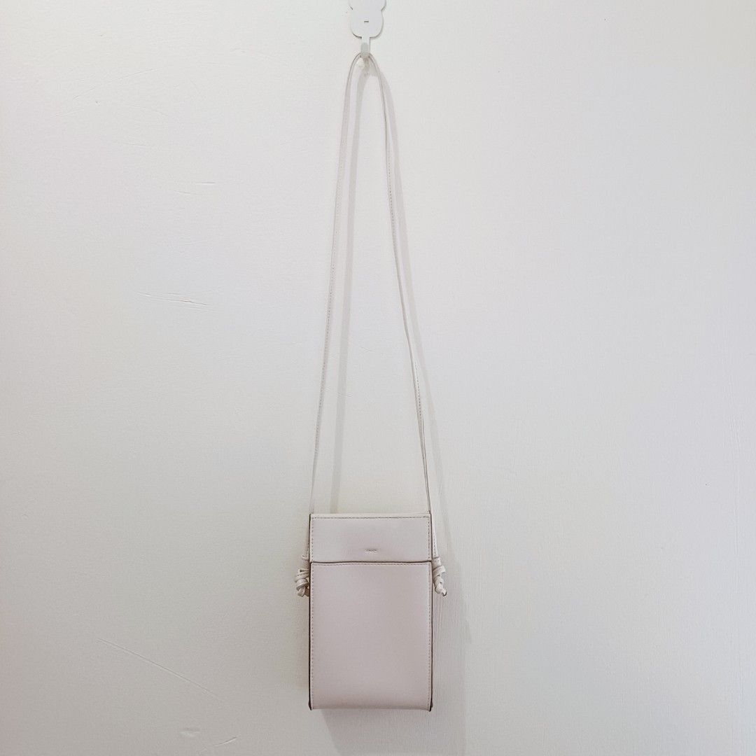 Sling bag from Uniqlo (Category: Cross-body Bags) located in Pasig City. Submitted by eden_online_shop (Listing ID 1470617938, Image 1). Description: - Color: Off white - Material: Faux leather - Design: Slim vertical profile with clean lines - Storage: Fits mobile phones and essential cards easily - Strap: Long, thin strap with stylish knotted ends - Style: Perfect match for casual everyday outfits - Condition: Well-maintained and in great shape