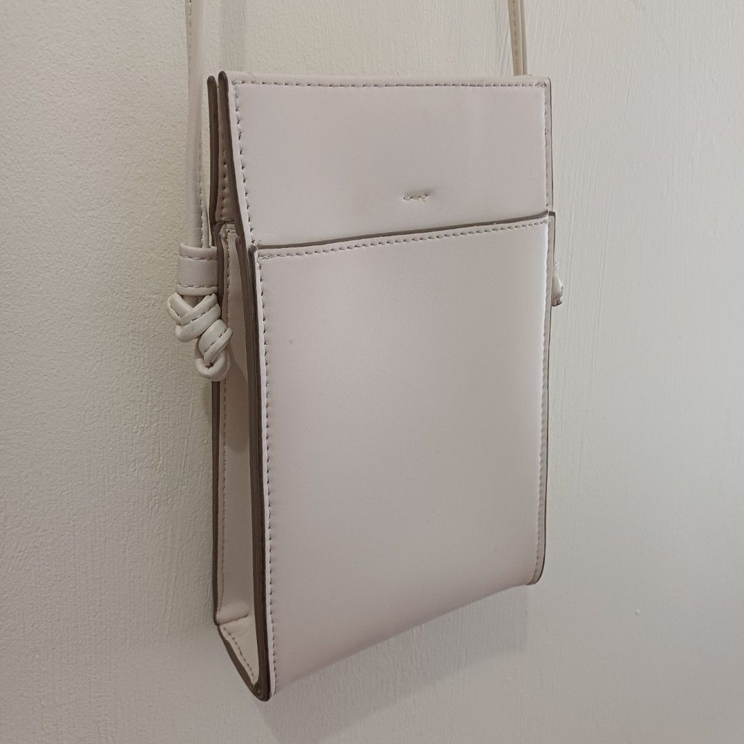 Sling bag from Uniqlo (Category: Cross-body Bags) located in Pasig City. Submitted by eden_online_shop (Listing ID 1470617938, Image 2). Description: - Color: Off white - Material: Faux leather - Design: Slim vertical profile with clean lines - Storage: Fits mobile phones and essential cards easily - Strap: Long, thin strap with stylish knotted ends - Style: Perfect match for casual everyday outfits - Condition: Well-maintained and in great shape