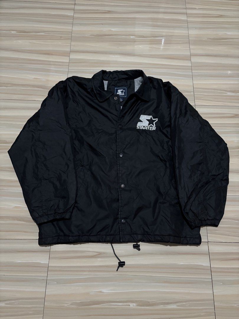 Starter Vintage Black Nylon Coach Jacket Size L (Category: Coats, Jackets and Outerwear) located in Ajuy. Submitted by reeyn0515 (Listing ID 1470708588, Image 1). Description: -25x29 - Brand: Starter Corp - Color: Solid black - Size: Large (L) - Design: Large embroidered logo patch on chest and oversized logo on the back - Features: Snap button front, collar, and adjustable drawstring hem - Lining: Grey jersey cotton lining for added warmth.