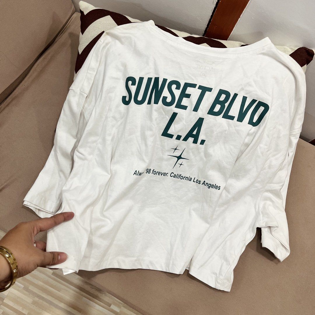 Sunset Blvd L.A. White Graphic Tee (Category: Tshirts & Polo Shirts ) located in Manila. Submitted by mjsappstopandshop (Listing ID 1470695525, Image 2). Description: White oversized t-shirt with dark green graphic print. Text reads on the front and back, with California Los Angeles lettering and star graphics below. Short sleeves, relaxed fit, comfy cotton material. Great casual piece for everyday wear..