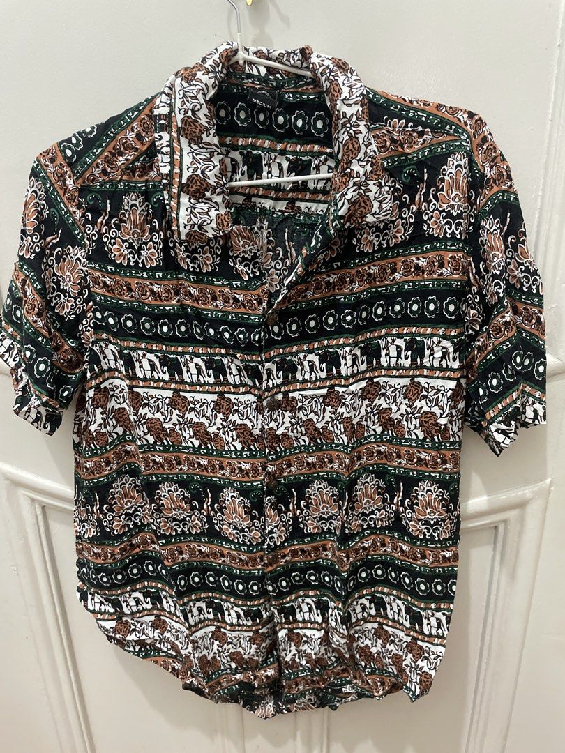 Thai Vintage style patterned short sleeve button-up shirt (Category: Tshirts & Polo Shirts ) located in Cainta. Submitted by nancygoreng (Listing ID 1470624431, Image 1). Description: - Size: Medium - Design: Intricate alternating horizontal bands of elephants, florals, and geometric motifs, from Thailand - Colors: Black base with green, white, and brown details - Features: Standard collar, front button closure, lightweight fabric - Perfect for: 
