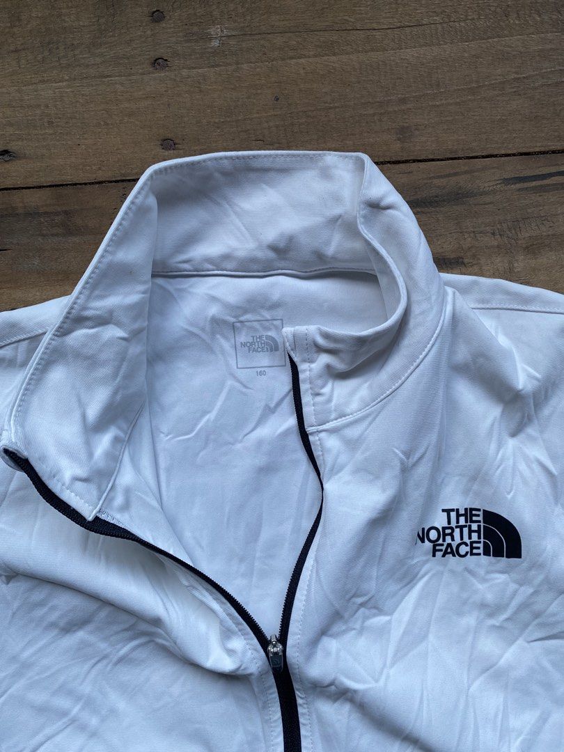 The North Face Never Stop Exploring White Track Jacket (Category: Coats, Jackets and Outerwear) located in Manila. Submitted by bravefox-98f5 (Listing ID 1470688732, Image 3). Description: - Brand: The North Face - Color: White with small black chest logo - Size: 160 (Youth/Petite friendly) - Design: Full zip, stand collar, and striking 'Never Stop Exploring' back lettering - Storage: Two secure front zip pockets - Fit: Ribbed cuffs and hem with 