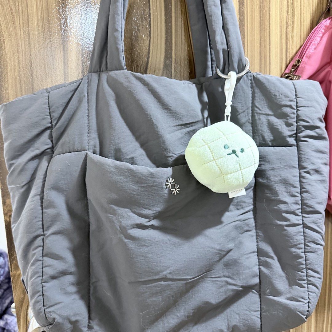 The Paper Bunny Puffer Shopper in Shadow (Category: Tote Bags) located in Manila. Submitted by juliaquindo (Listing ID 1470563231, Image 2). Description: - Brand: The Paper Bunny - Color: Dark grey - Material: Quilted fabric body - Features: Comfortable shoulder straps, front pocket with flower pin detail, and a green melon plush keychain - Condition: Clean inside and out - Capacity: Roomy daily bag that easily fits all your essentials.