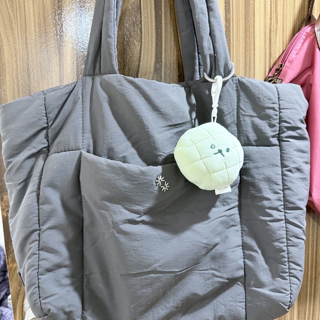 The Paper Bunny Puffer Shopper in Shadow (Category: Tote Bags) located in Manila. Submitted by juliaquindo (Listing ID 1470563231, Image 3). Description: - Brand: The Paper Bunny - Color: Dark grey - Material: Quilted fabric body - Features: Comfortable shoulder straps, front pocket with flower pin detail, and a green melon plush keychain - Condition: Clean inside and out - Capacity: Roomy daily bag that easily fits all your essentials.