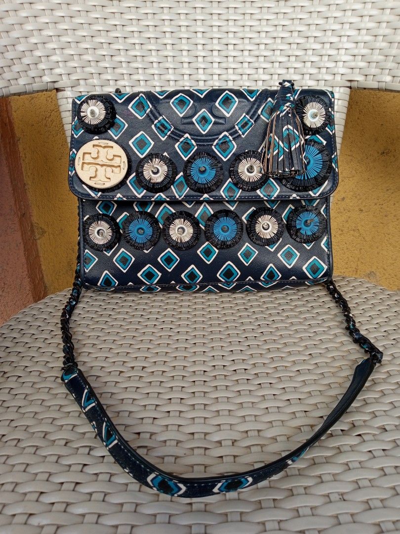 Tory Burch Geometric Pattern Flap Shoulder Bag with Embellishments (Category: Luxury Bags & Wallets) located in Liloan. Submitted by dnznoon31 (Listing ID 1470599715, Image 1). Description: - Brand: Tory Burch - Design: Navy blue with geometric diamond print, fringed circular appliques, large cream logo medallion, and matching tassel - Strap: Dark chain and leather combination - - Interior: Navy fabric lining with a convenient zippered pocket and