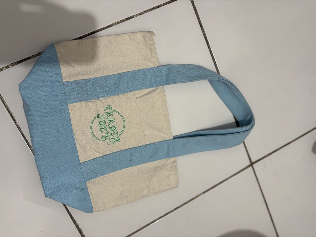 Trader Joe's mini Blue Canvas Tote Bag (Category: Tote Bags) located in Taguig. Submitted by cftbncs (Listing ID 1470560597, Image 2). Description: - Authentic Trader Joe's canvas tote bag - Colorway: Cream body with stylish light blue handles and bottom panel - Features a green embroidered Trader Joe's logo on the front pocket - Made from durable, heavy-duty cotton canvas - Equipped with sturdy double straps for comfortable carrying - Spacious s