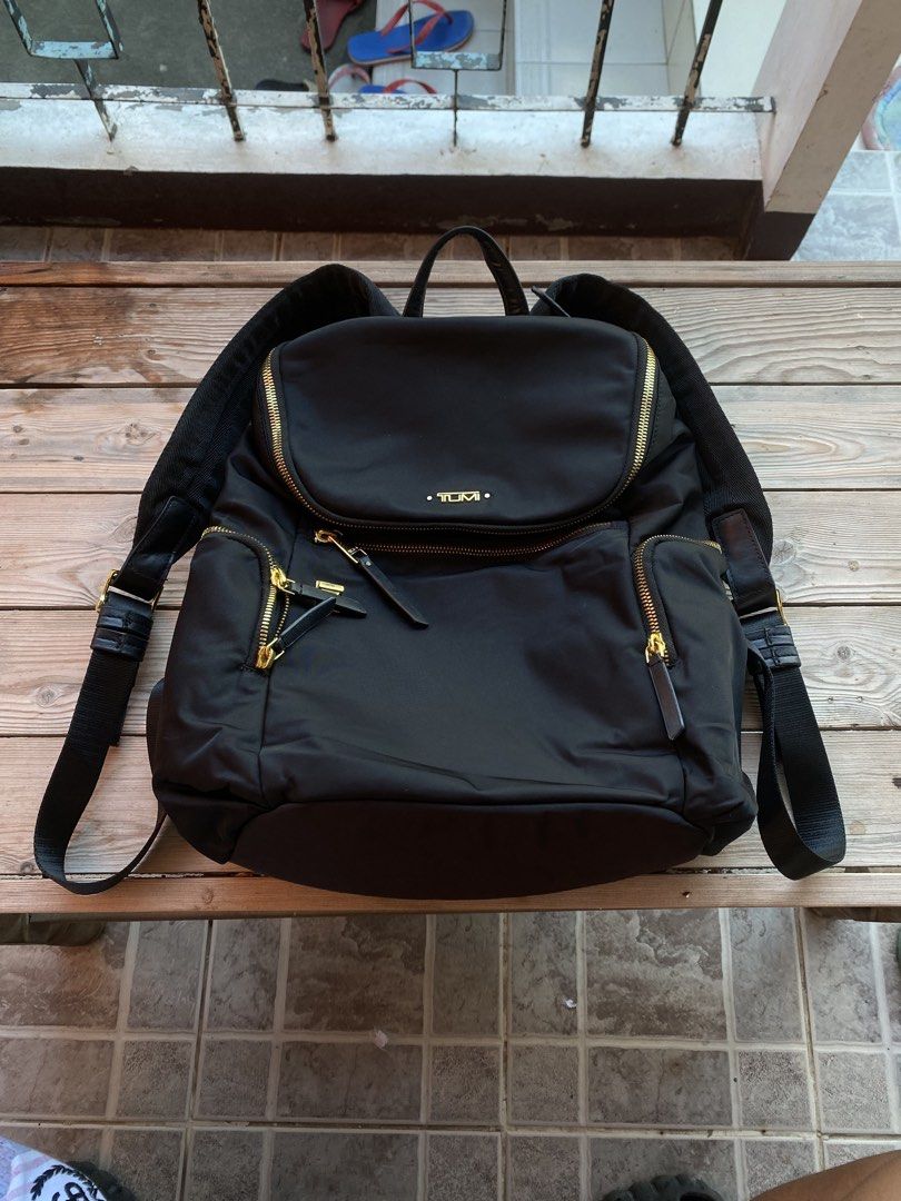 TUMI Black Nylon Backpack with Gold Hardware (Category: Backpacks) located in San Fernando. Submitted by thrifteezy6 (Listing ID 1470635424, Image 2). Description: - Authentic TUMI black nylon backpack - Elegant gold-tone zippers and hardware - Top handle and comfortable adjustable shoulder straps - Front zip pocket with stylish leather zipper pulls - Spacious main compartment with interior organization pockets (zip and slip pockets) - Light grey
