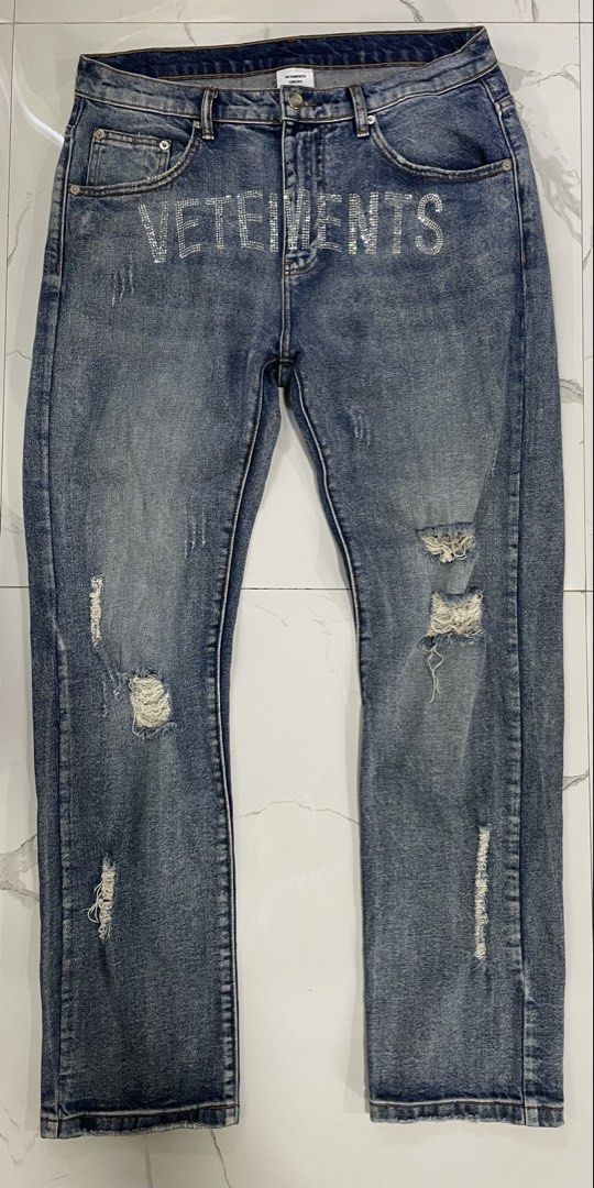 Vetemets Rhinestone Distressed Denim Jeans (Category: Jeans) located in Calapan. Submitted by lucasthrifts (Listing ID 1470569577, Image 1). Description: - Brand/Model: Vetemets Unisex Denim Jeans (Hiver 2021) - Size: 31 - Color/Wash: Mid-blue wash - Design Details: Rhinestone lettering across the front, distressed rips on both legs - Features: Standard button fly, classic five-pocket design, and paper brand patch with handwritten lettering .