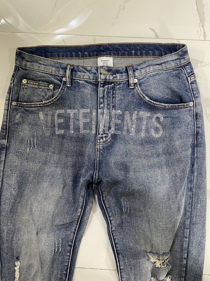 Vetemets Rhinestone Distressed Denim Jeans (Category: Jeans) located in Calapan. Submitted by lucasthrifts (Listing ID 1470569577, Image 3). Description: - Brand/Model: Vetemets Unisex Denim Jeans (Hiver 2021) - Size: 31 - Color/Wash: Mid-blue wash - Design Details: Rhinestone lettering across the front, distressed rips on both legs - Features: Standard button fly, classic five-pocket design, and paper brand patch with handwritten lettering .