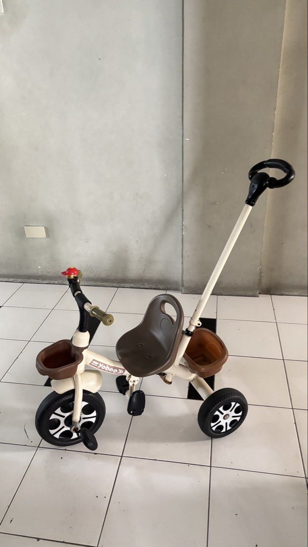 Yoboo Toddler Tricycle with Push Handle and Baskets (Category: Infant Playtime) located in Manila. Submitted by calliope777 (Listing ID 1470608228, Image 1). Description: - Brand/Model: Yoboo toddler tricycle - Color: Cream and brown - Frame: Sturdy metal frame for safe neighborhood rides - Comfort & Safety: Plastic seat with backrest and front wheel foot pedals - Control: Parent push handle on the back - Storage: Front basket and rear storage bu