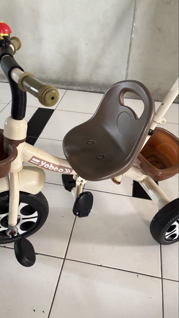 Yoboo Toddler Tricycle with Push Handle and Baskets (Category: Infant Playtime) located in Manila. Submitted by calliope777 (Listing ID 1470608228, Image 3). Description: - Brand/Model: Yoboo toddler tricycle - Color: Cream and brown - Frame: Sturdy metal frame for safe neighborhood rides - Comfort & Safety: Plastic seat with backrest and front wheel foot pedals - Control: Parent push handle on the back - Storage: Front basket and rear storage bu