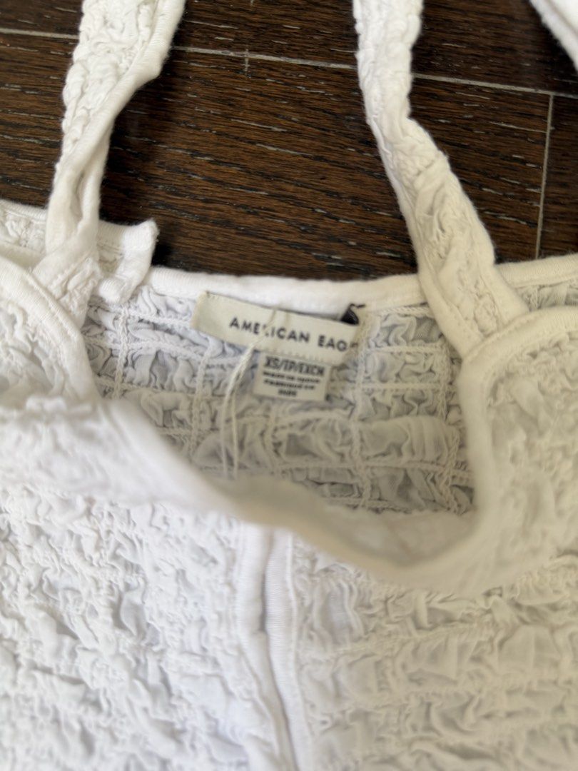 American Eagle White Smocked Crop Top Size XS (Category: Sleeveless) located in Manila. Submitted by shopmnl.studio (Listing ID 1470781510, Image 2). Description: - Brand: American Eagle - Size: XS (Super stretchy material) - Color: White - Details: Textured crinkled fabric, thick straps, split front hem - Style tip: Perfect for pairing with high-waisted jeans or skirts.
