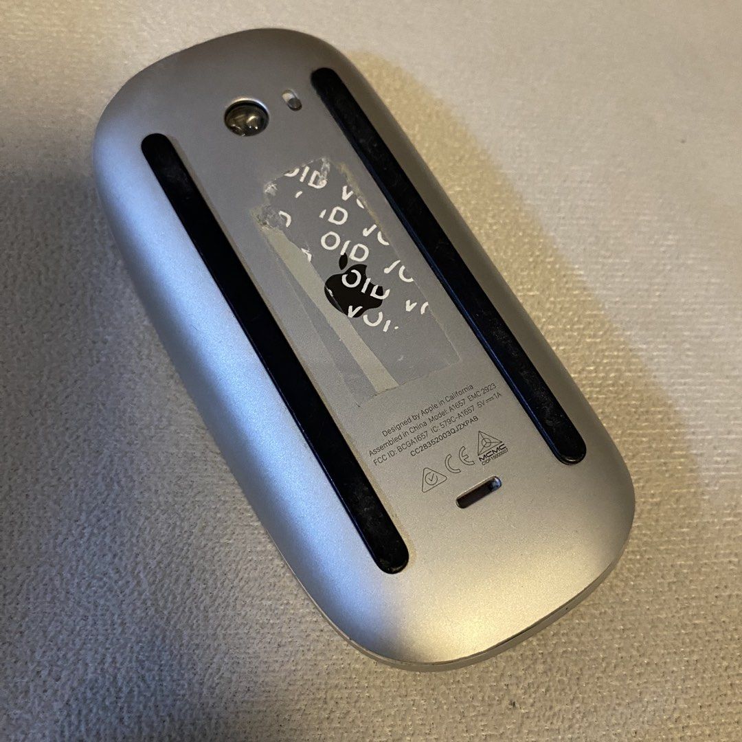 Apple Magic Mouse Model A1657 (Category: Mouse & Mousepads) located in Santa Rosa. Submitted by dasha07 (Listing ID 1470869755, Image 3). Description: - Model: Apple Magic Mouse A1657 - Condition: Fully functional, connects seamlessly via Bluetooth - Design: Silver aluminum base with a clean white top surface and Apple logo - Power: Rechargeable battery with port located underneath - Flaws: Bottom shows standard wear and tear with peeling on the 